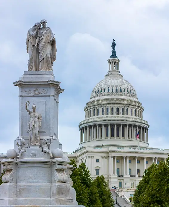 The Peace Monument in foreground with the United States Capitol dome under a cloudy sky in Washington, D.C.