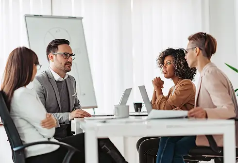 Four professionals in business attire engaged in a collaborative meeting around a white table in a bright office.